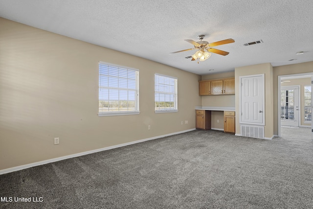 unfurnished living room with carpet, visible vents, baseboards, built in desk, and a textured ceiling