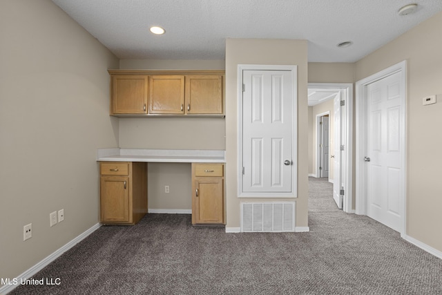 kitchen featuring baseboards, visible vents, dark carpet, and built in study area