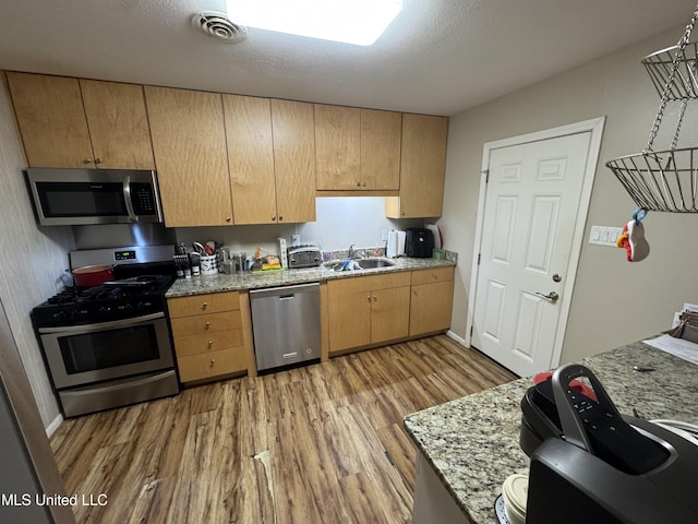 15708 Orleans Dr, Biloxi, MS 39532 - kitchen featuring appliances with stainless steel finishes, light wood-style flooring, light stone counters, light brown cabinets, and a textured ceiling