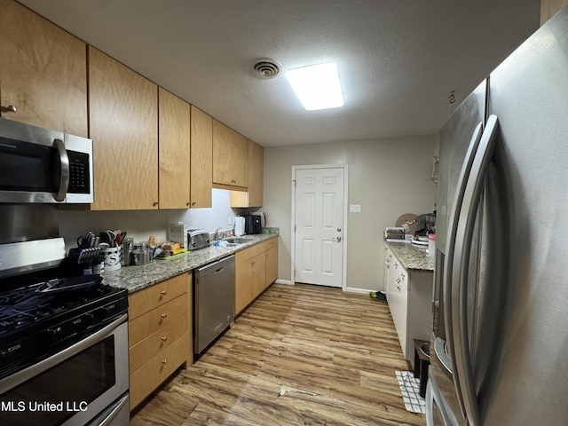 15708 Orleans Dr, Biloxi, MS 39532 - kitchen featuring appliances with stainless steel finishes, light wood-style floors, light brown cabinets, a textured ceiling, and light stone counters