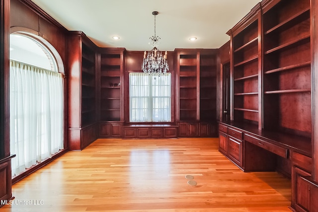 unfurnished office featuring plenty of natural light, built in desk, light hardwood / wood-style floors, and an inviting chandelier