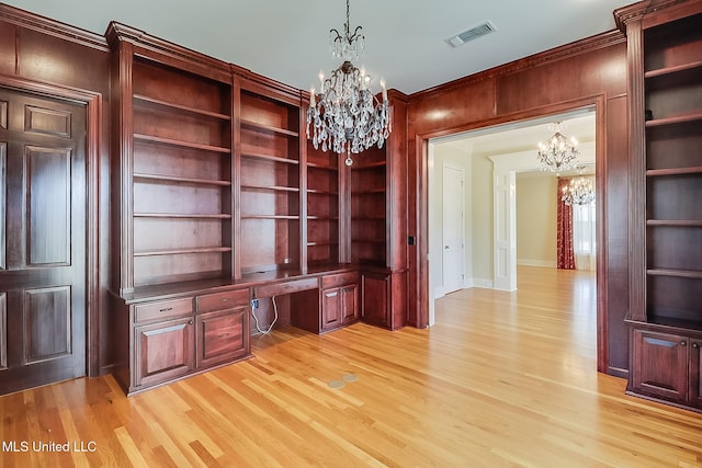 unfurnished office with built in desk, built in features, an inviting chandelier, light hardwood / wood-style floors, and wood walls