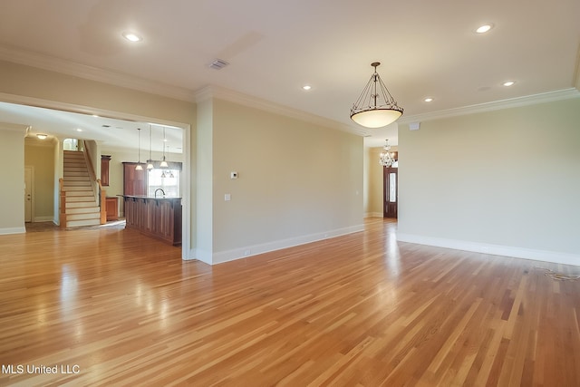 empty room featuring an inviting chandelier, ornamental molding, and light wood-type flooring