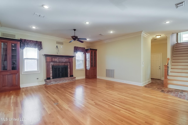 unfurnished living room featuring a brick fireplace, crown molding, ceiling fan, and light wood-type flooring