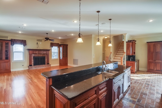 kitchen featuring sink, hanging light fixtures, a brick fireplace, crown molding, and a kitchen island with sink