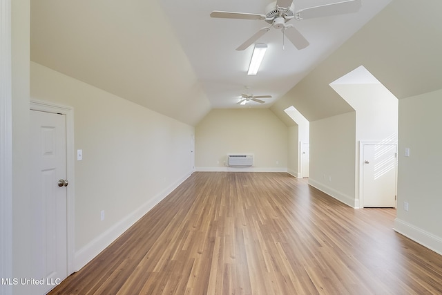 additional living space with ceiling fan, light wood-type flooring, a wall unit AC, and vaulted ceiling