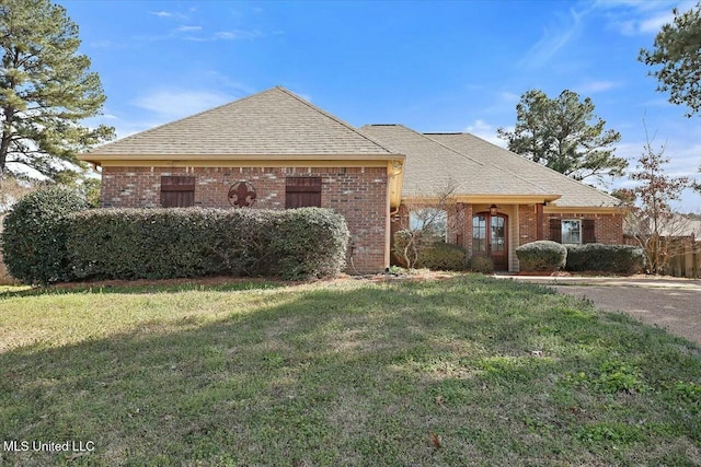 view of front of property featuring brick siding, roof with shingles, and a front yard