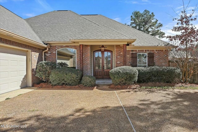 doorway to property with brick siding, a shingled roof, and french doors