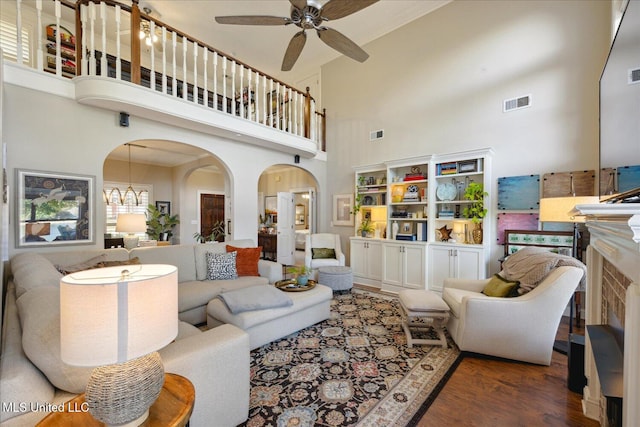 living room featuring a high ceiling, a fireplace, dark hardwood / wood-style flooring, and ceiling fan with notable chandelier