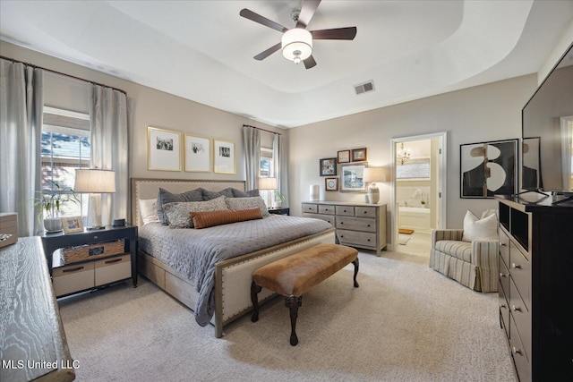 bedroom with ceiling fan, multiple windows, connected bathroom, and a tray ceiling