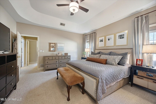 carpeted bedroom with ceiling fan and a tray ceiling