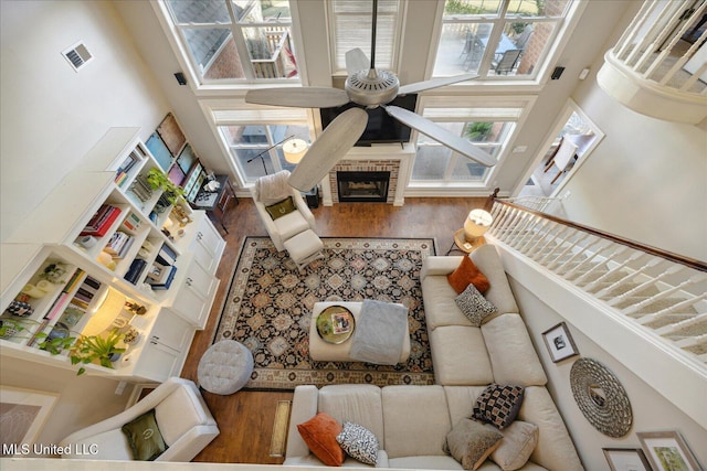 living room with a high ceiling, hardwood / wood-style flooring, a wall mounted air conditioner, ceiling fan, and a fireplace