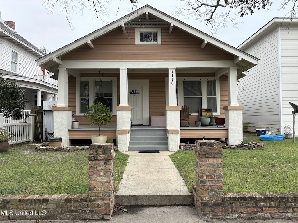 bungalow-style house featuring covered porch, a front yard, and fence