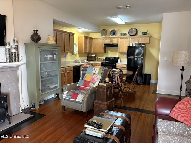 living room with dark wood-type flooring, a wood stove, baseboards, and visible vents