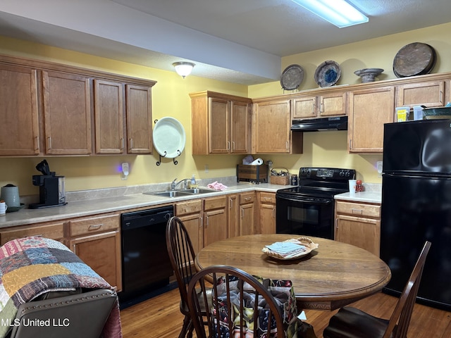 kitchen with under cabinet range hood, black appliances, light countertops, and a sink