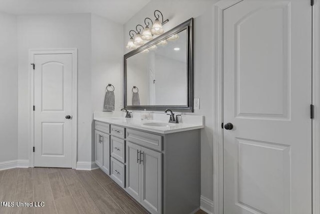 bathroom with double vanity, baseboards, a sink, and wood finished floors