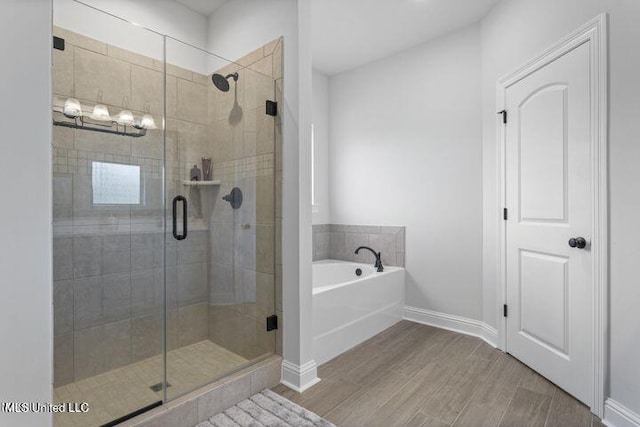 bathroom with a stall shower, a garden tub, baseboards, and wood finished floors