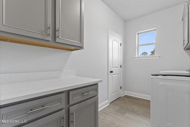 laundry room featuring baseboards, cabinet space, washing machine and clothes dryer, and light wood finished floors