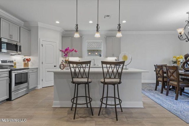 kitchen with a breakfast bar area, appliances with stainless steel finishes, a kitchen island, and gray cabinets