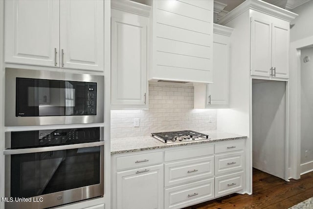 kitchen with appliances with stainless steel finishes, tasteful backsplash, white cabinets, dark hardwood / wood-style flooring, and light stone countertops