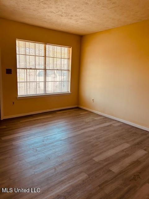 unfurnished room with dark wood-type flooring, a textured ceiling, and baseboards