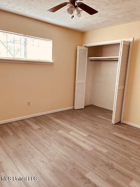 unfurnished bedroom featuring light wood-style flooring, a closet, baseboards, and a textured ceiling