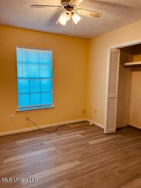 unfurnished bedroom with baseboards, ceiling fan, wood finished floors, a textured ceiling, and a closet