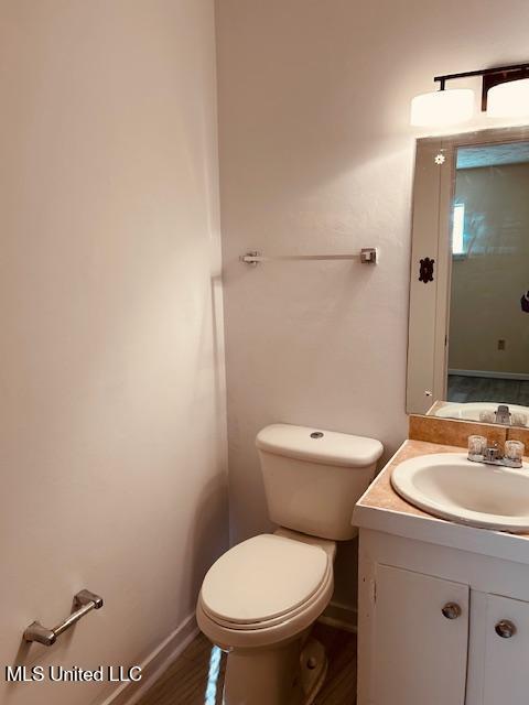 half bath with toilet, baseboards, wood finished floors, and vanity