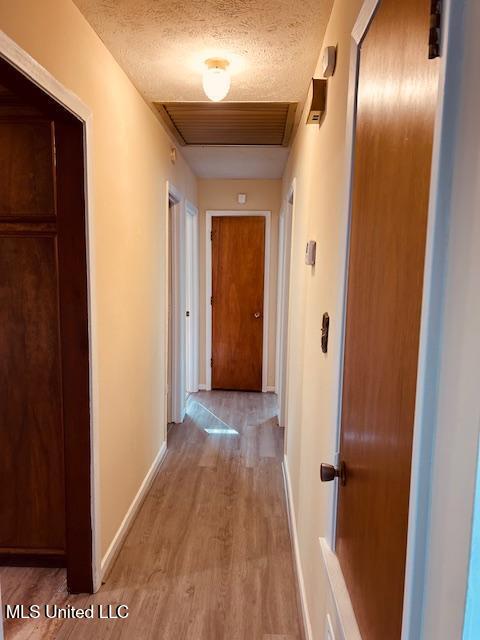 hall with a textured ceiling, light wood-type flooring, visible vents, and baseboards