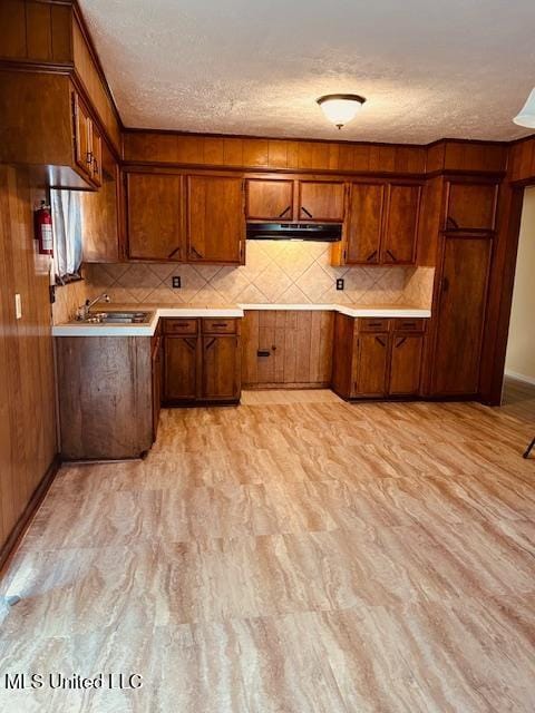 kitchen with light wood-type flooring, decorative backsplash, brown cabinets, and light countertops