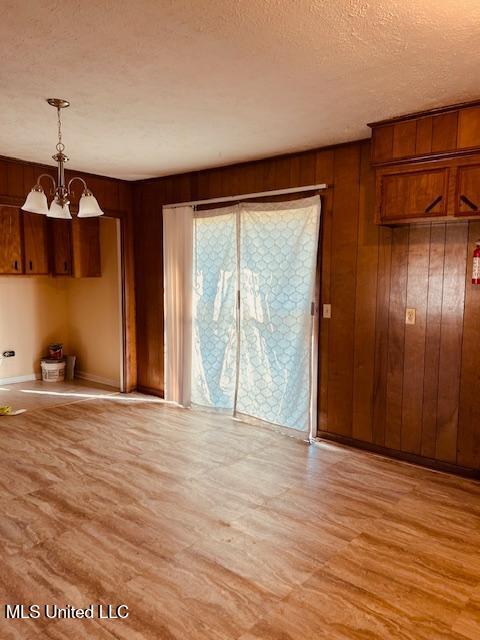 unfurnished dining area featuring light wood-style flooring, a textured ceiling, wooden walls, and an inviting chandelier