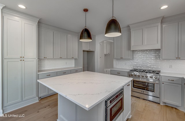 kitchen with a center island, light wood-type flooring, decorative light fixtures, stainless steel appliances, and light stone counters