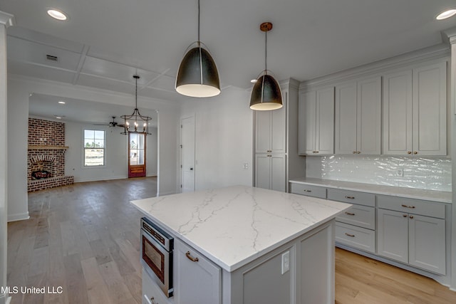 kitchen with pendant lighting, stainless steel microwave, tasteful backsplash, light stone countertops, and a kitchen island