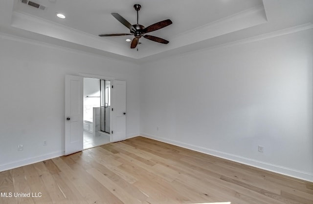 spare room featuring ornamental molding, light wood-type flooring, and a raised ceiling