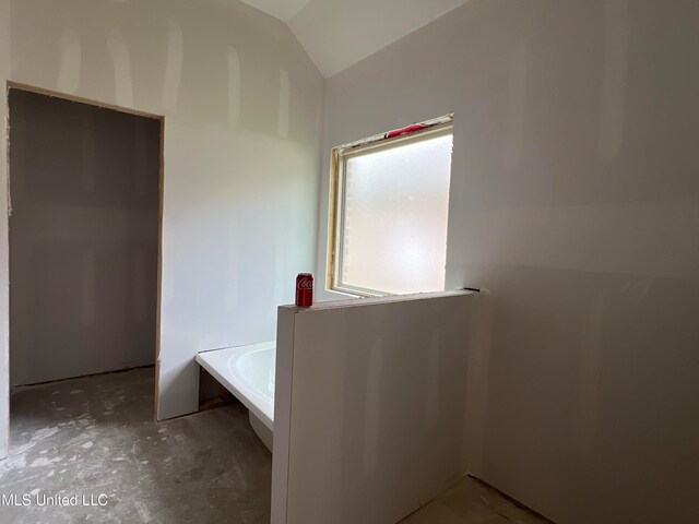 bathroom with a tub to relax in and lofted ceiling