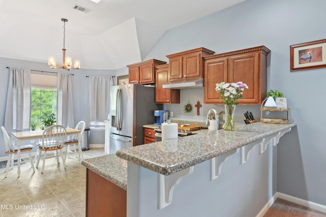 2301 Paula Cir, Ocean Springs, MS 39564 - kitchen with under cabinet range hood, brown cabinets, stainless steel fridge, a breakfast bar, and lofted ceiling