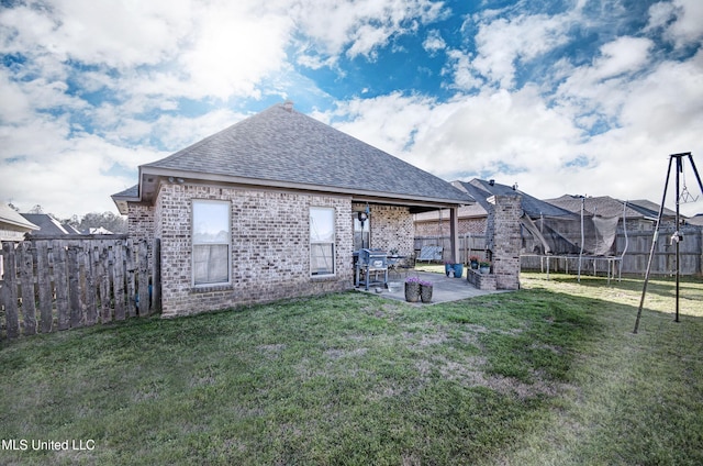 back of house with a fenced backyard, a lawn, a patio, and a trampoline