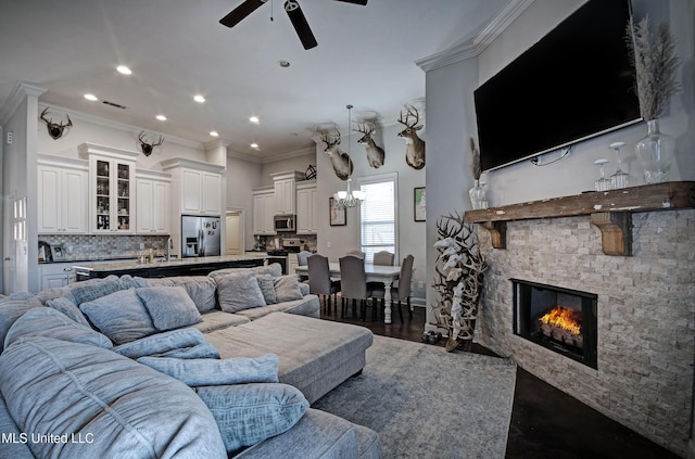 living area with a ceiling fan, dark wood-type flooring, ornamental molding, and a fireplace