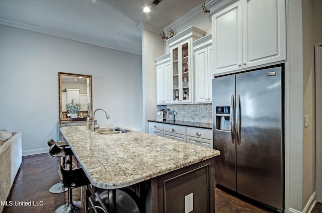 kitchen featuring an island with sink, a sink, stainless steel fridge, crown molding, and decorative backsplash