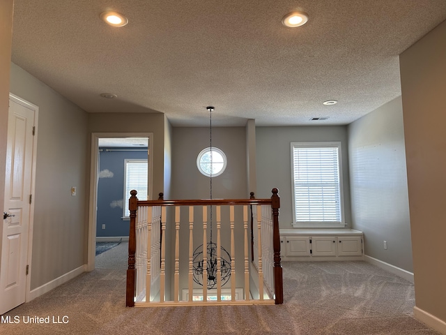 hallway with a textured ceiling, light carpet, and a wealth of natural light