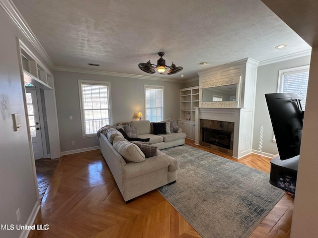 living room featuring a tile fireplace, ceiling fan, parquet flooring, a textured ceiling, and ornamental molding