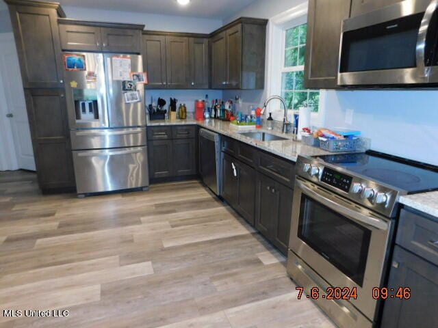 kitchen featuring light stone countertops, appliances with stainless steel finishes, sink, light hardwood / wood-style floors, and dark brown cabinetry