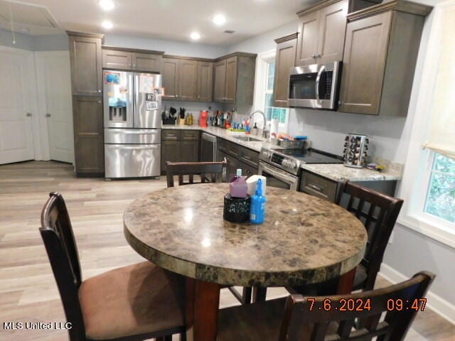 kitchen featuring stainless steel appliances, sink, light stone counters, and light wood-type flooring