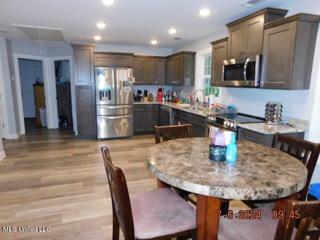 kitchen featuring light stone countertops, light hardwood / wood-style flooring, stainless steel appliances, sink, and a center island