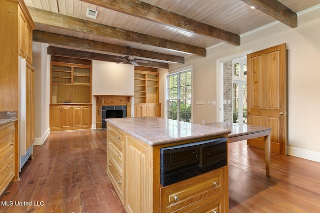 kitchen with beam ceiling, ceiling fan, a center island, a tiled fireplace, and wood ceiling