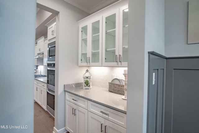 kitchen with tasteful backsplash, light hardwood / wood-style flooring, crown molding, white cabinets, and appliances with stainless steel finishes