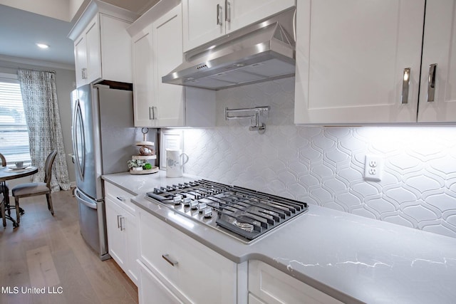 kitchen featuring white cabinets, light stone countertops, appliances with stainless steel finishes, and light hardwood / wood-style flooring