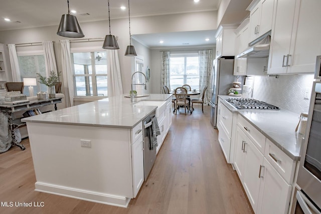 kitchen with white cabinetry, tasteful backsplash, light stone counters, decorative light fixtures, and a kitchen island with sink