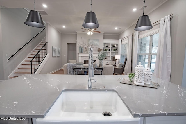 kitchen with light stone countertops, crown molding, sink, decorative light fixtures, and built in features