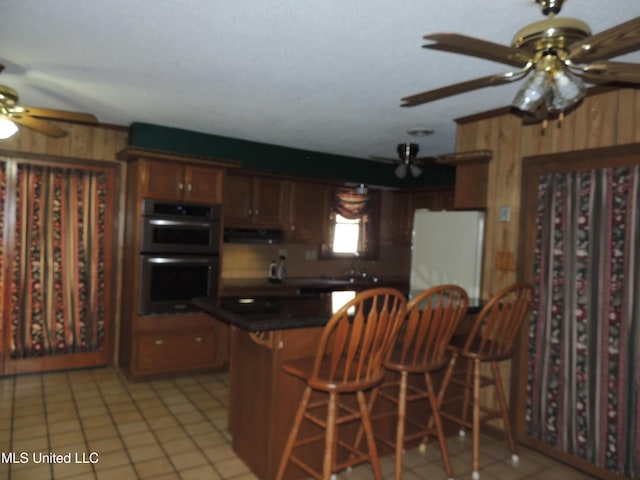 kitchen featuring double oven, white refrigerator, kitchen peninsula, ceiling fan, and light tile patterned floors